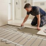 A person installs an electric underfloor heating system beneath tiles.